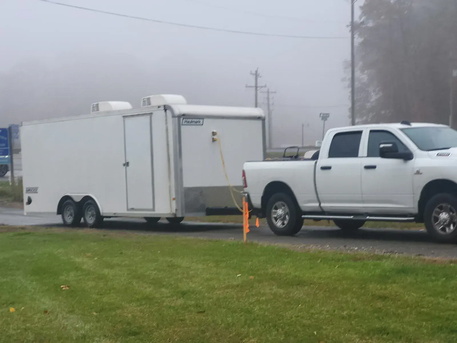 A white pickup truck towing a white enclosed transport trailer on a foggy morning